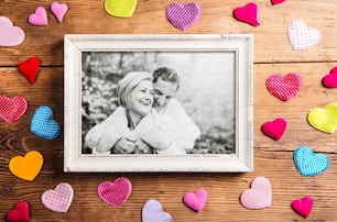 Black and white photo of seniors in autumn nature, colorful fabric hearts surrounding it. Studio shot on brown wooden background.