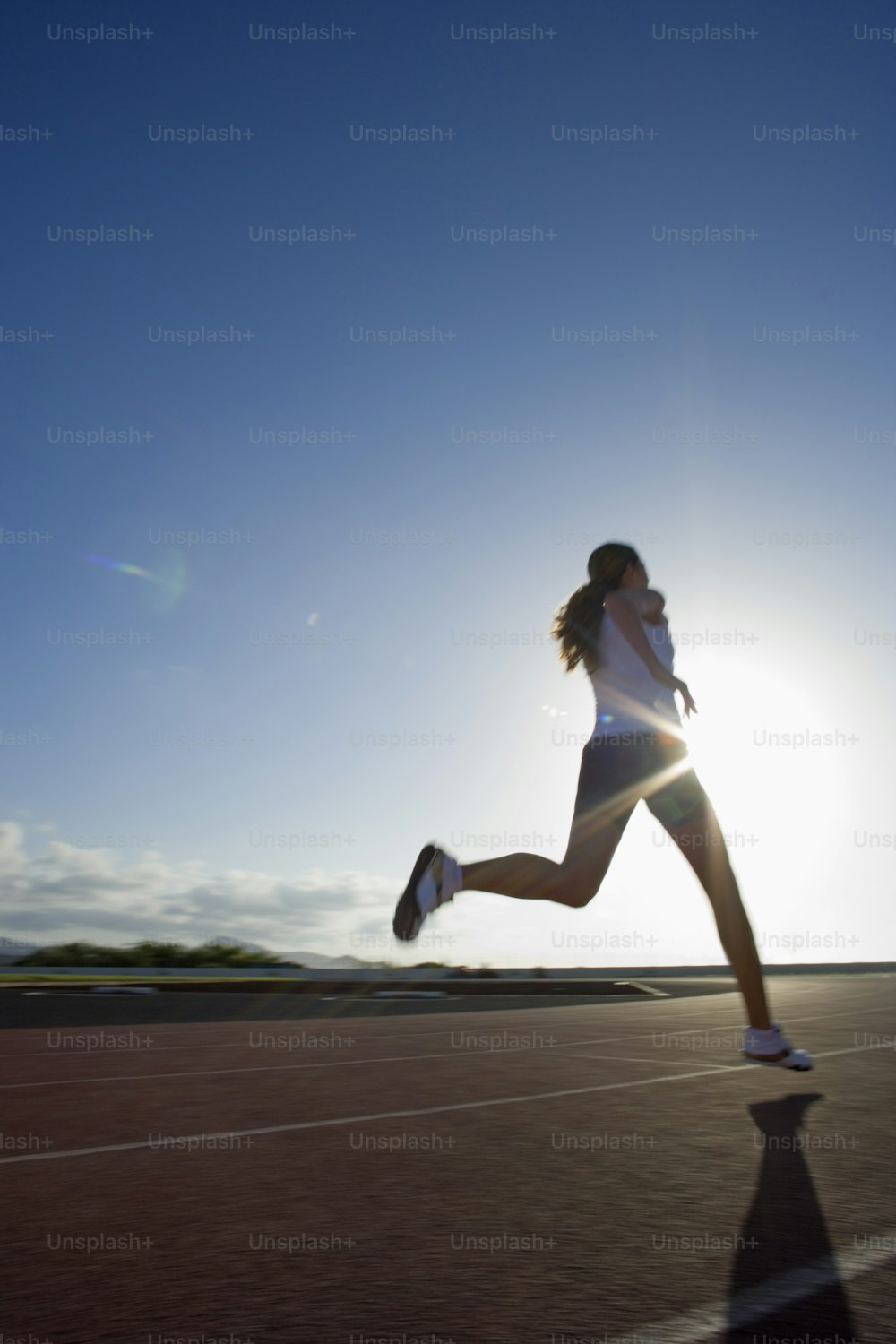 a woman running on a road with the sun in the background