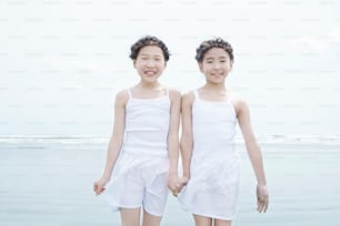 two young girls standing next to each other on a beach