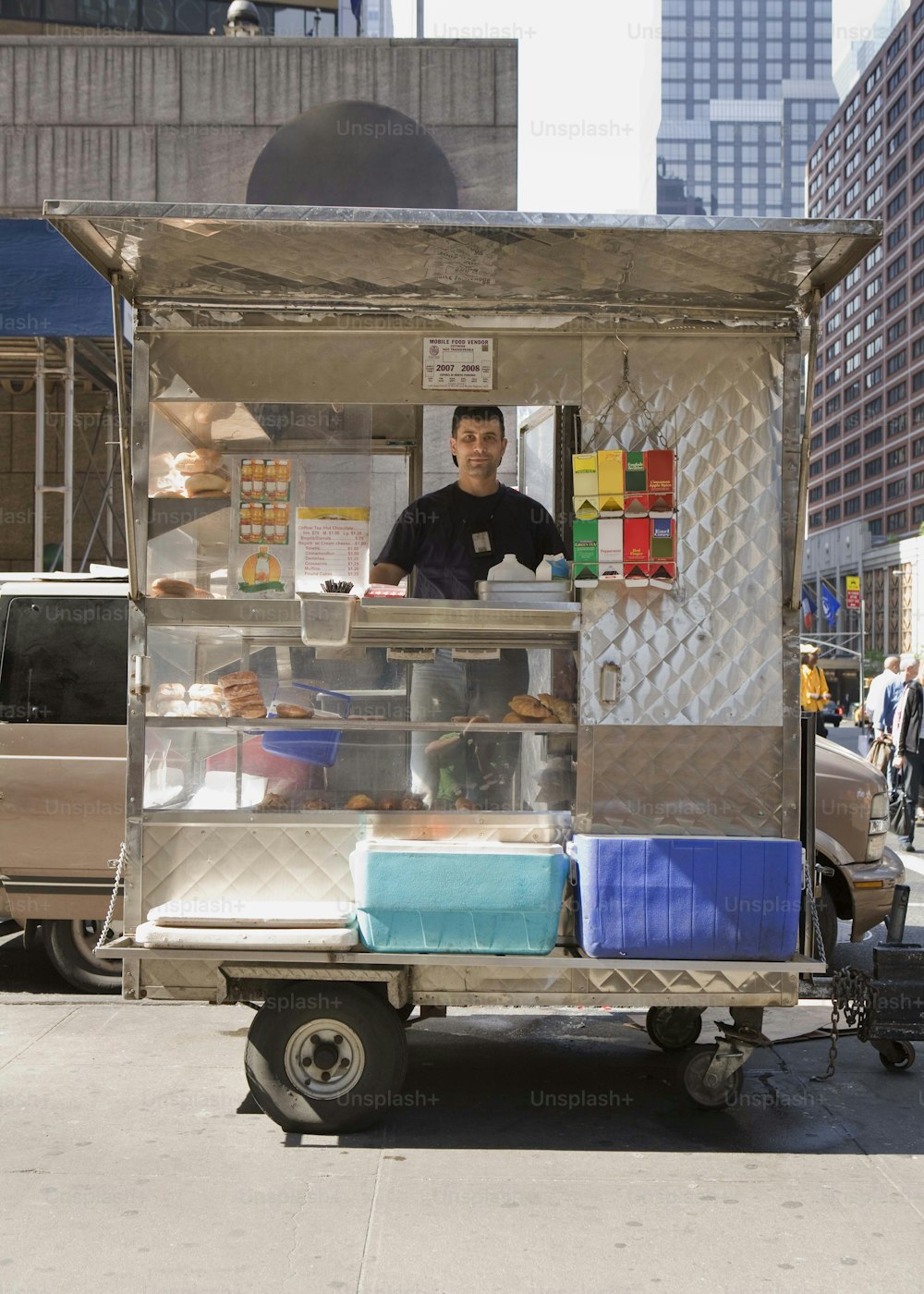 a man standing behind a food cart on a city street