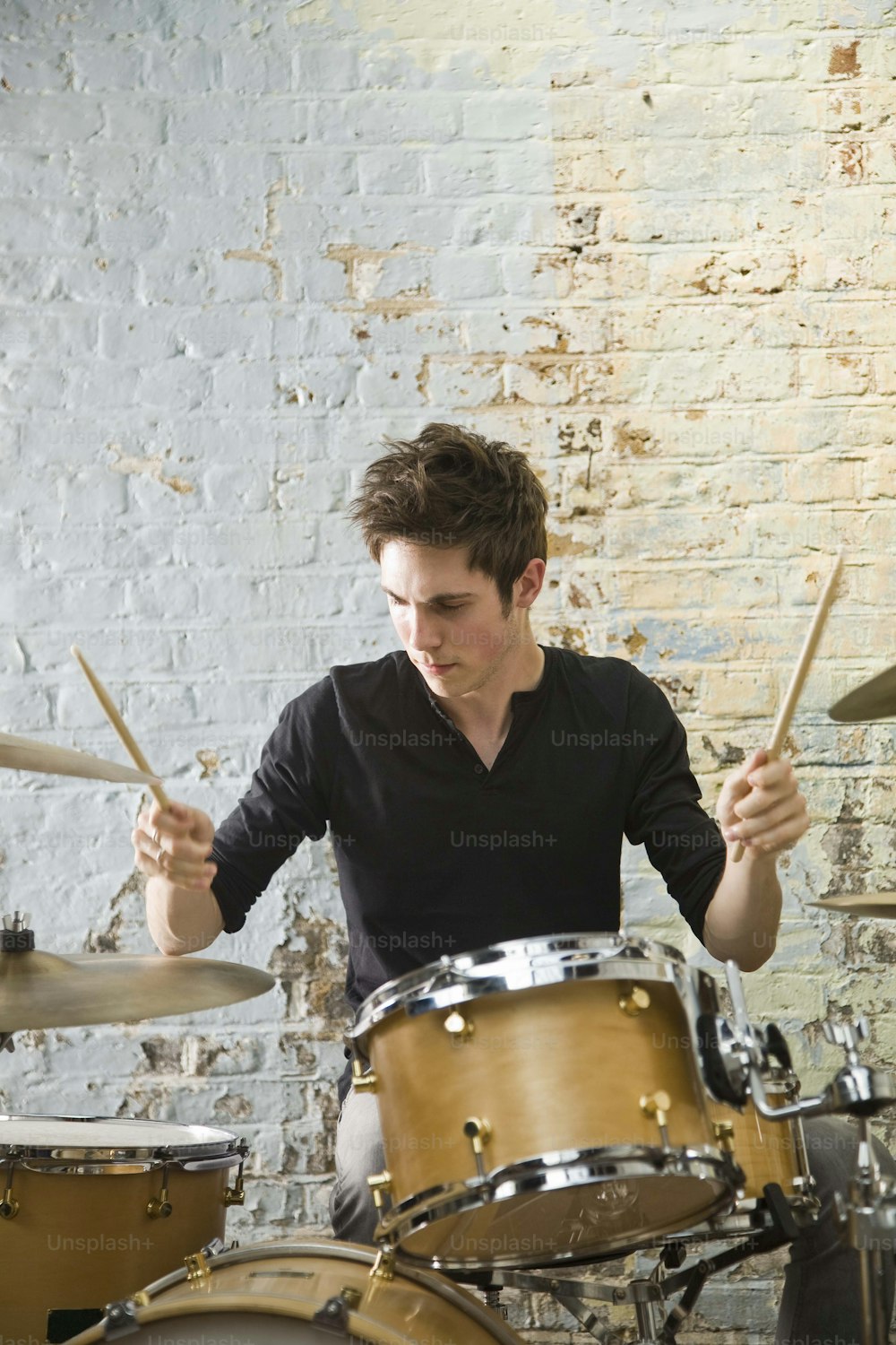 a man playing drums in front of a brick wall