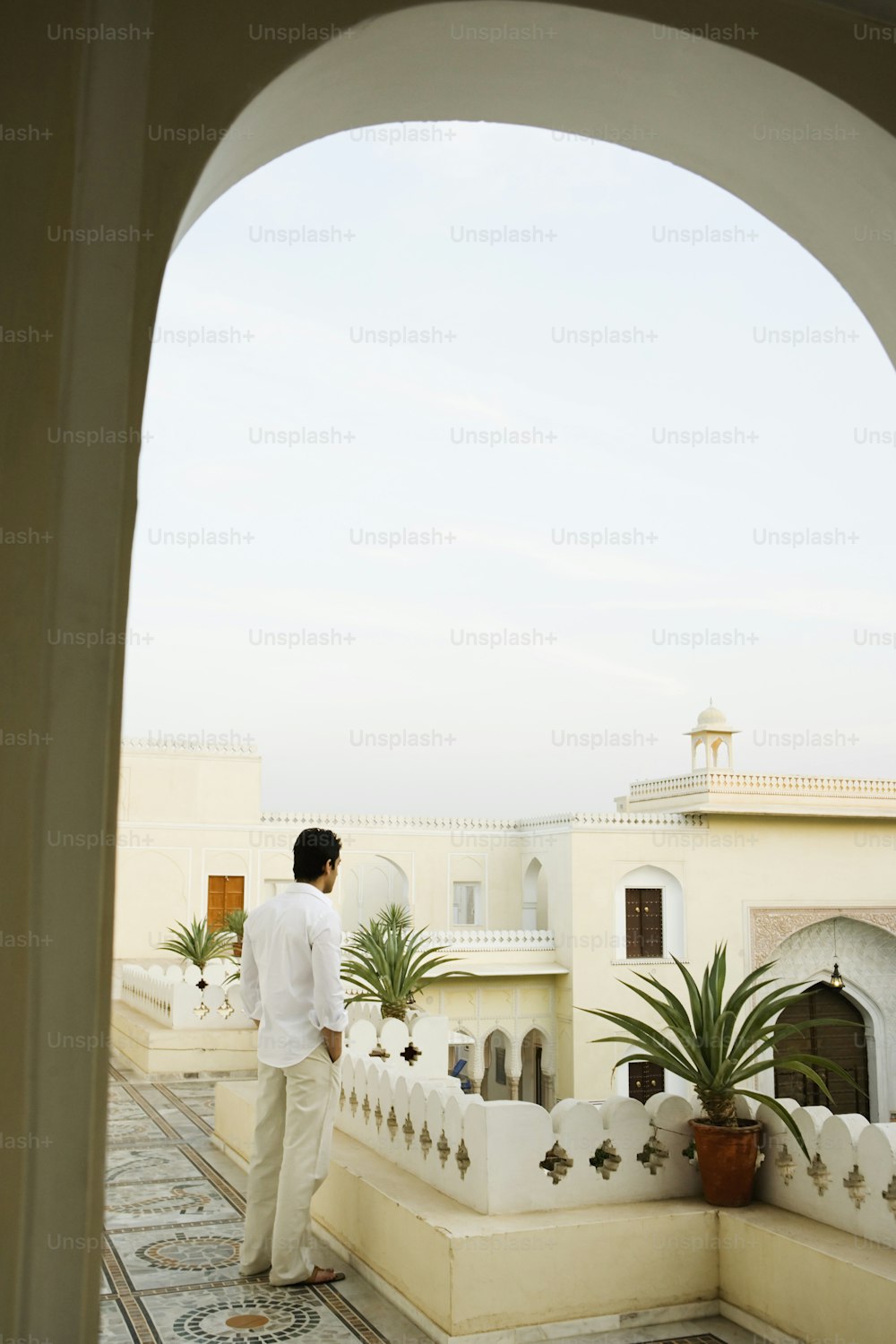 Un hombre parado en un balcón junto a una planta en maceta