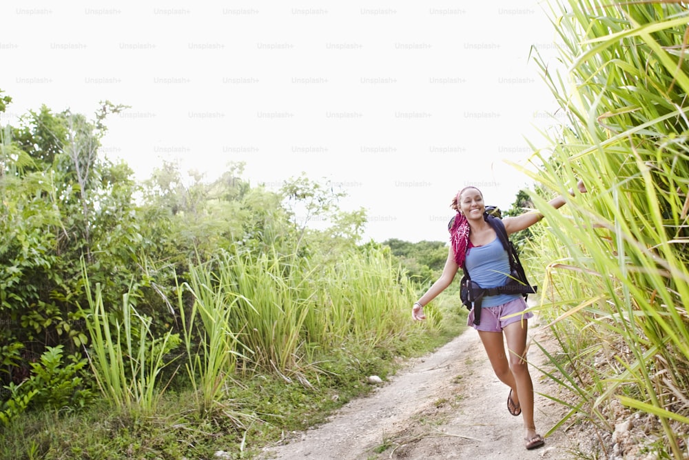 a woman walking down a dirt road next to tall grass