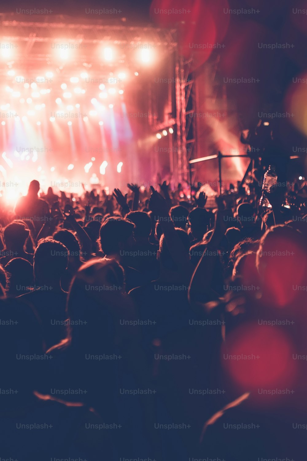 眩しいステージライトの前に集まったフェスティバルコンサートの群衆のシルエット。見分けがつかない人物とカラフルな効果。
