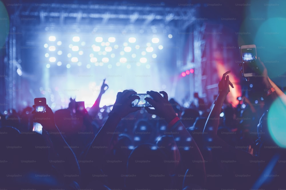 Silhouettes de la foule des concerts du festival devant les lumières vives de la scène. Des personnes méconnaissables et des effets colorés.