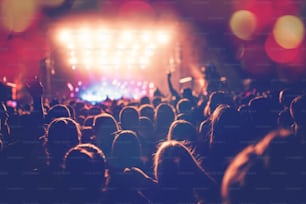 Silhouettes of festival concert crowd in front of bright stage lights. Unrecognizable people and colorful effects.