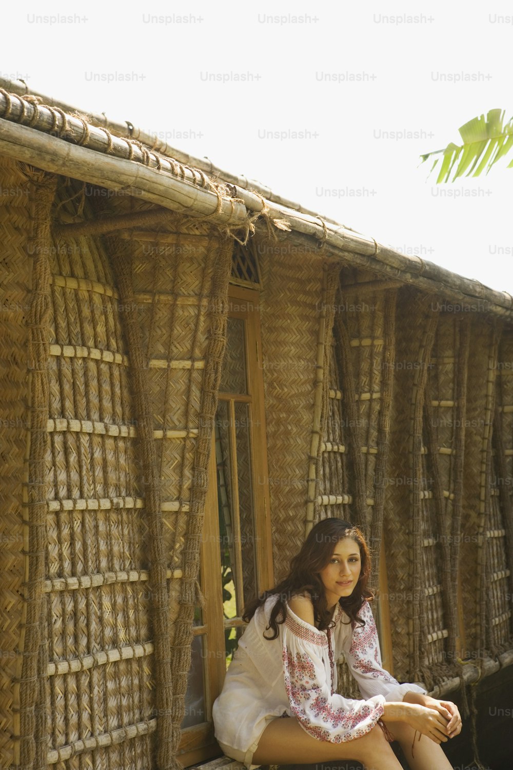 a woman sitting on a bench in front of a hut