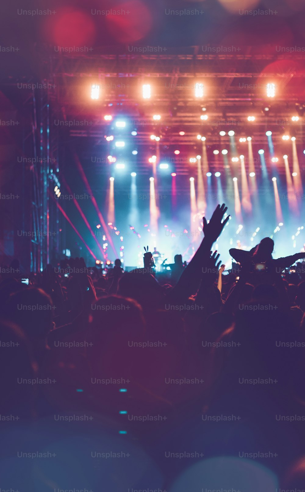 Silhouettes of festival concert crowd in front of bright stage lights. Unrecognizable people and colorful effects.