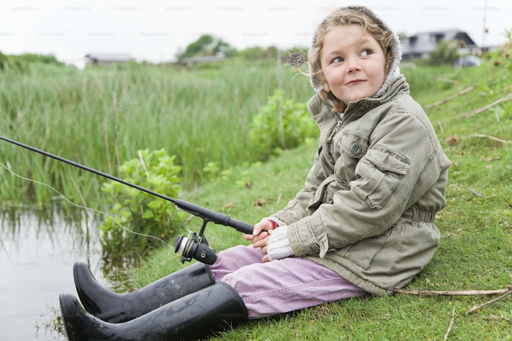 a little girl sitting on the ground with a fishing rod