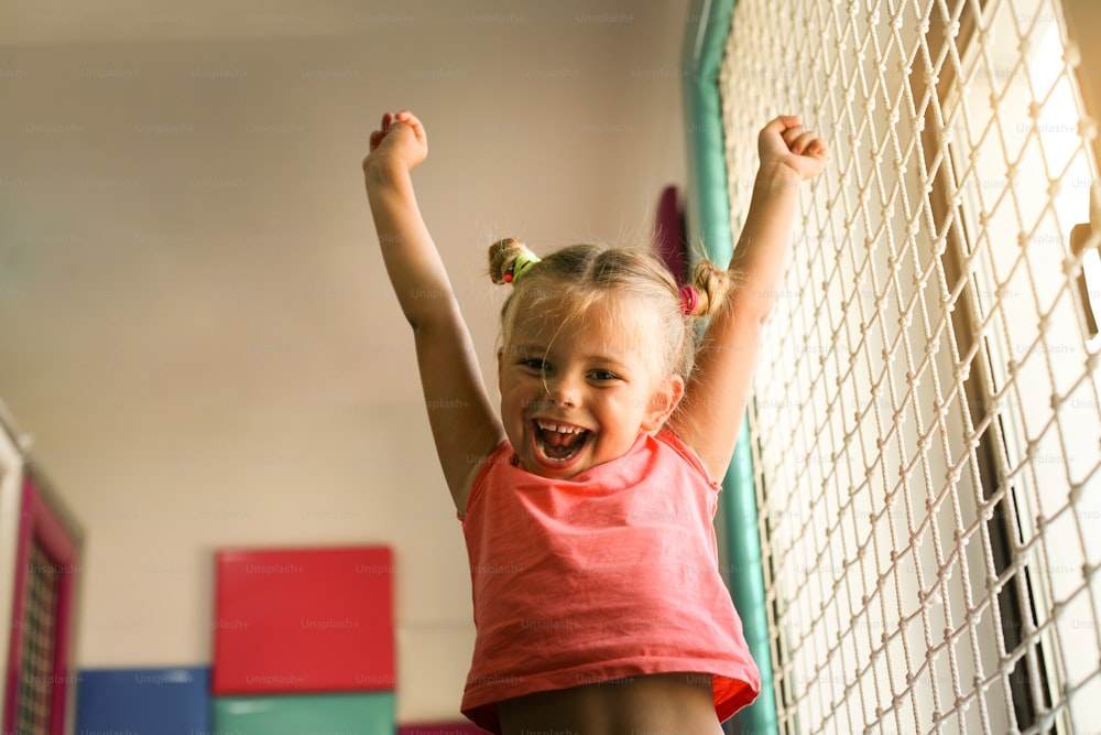 Menina no playground. Menina feliz com os braços levantados olhando para a câmera.