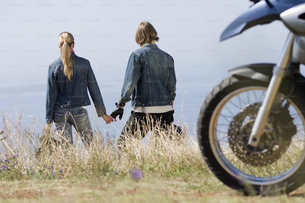 a man and a woman holding hands while standing next to a motorcycle