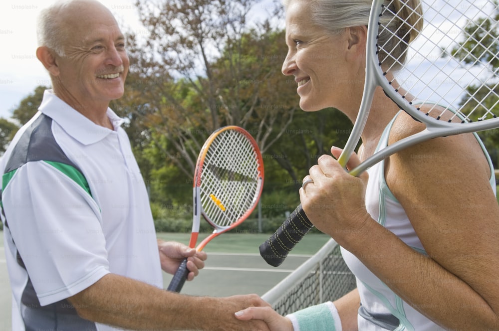 um homem e uma mulher apertando as mãos sobre uma raquete de tênis