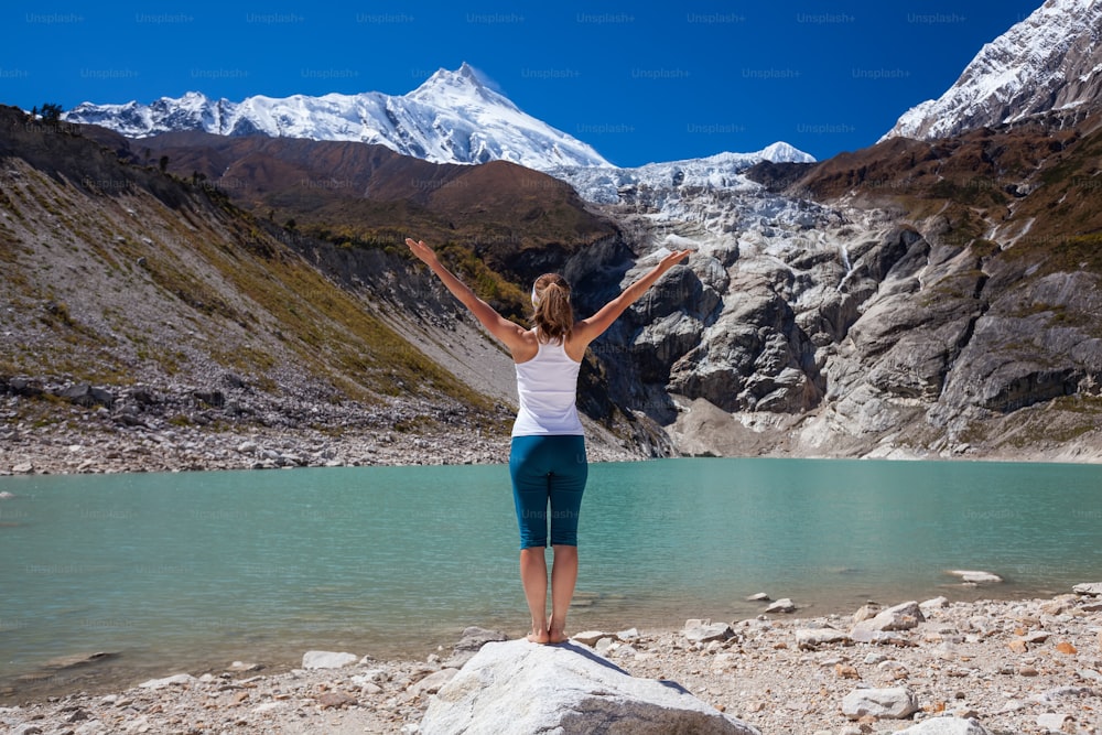 Woman is doing yoga excercises near big lake on the Manaslu circuit trak in Nepala