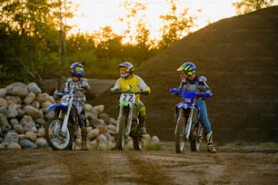 three people on dirt bikes on a dirt road