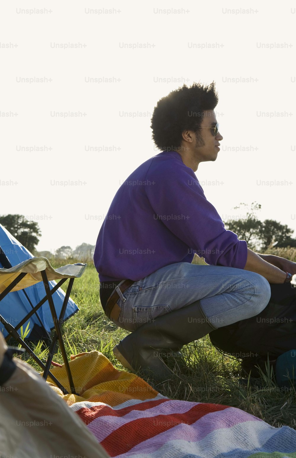 a man sitting on top of a blanket next to a camping chair