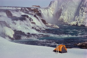 a tent pitched up in the snow next to a waterfall