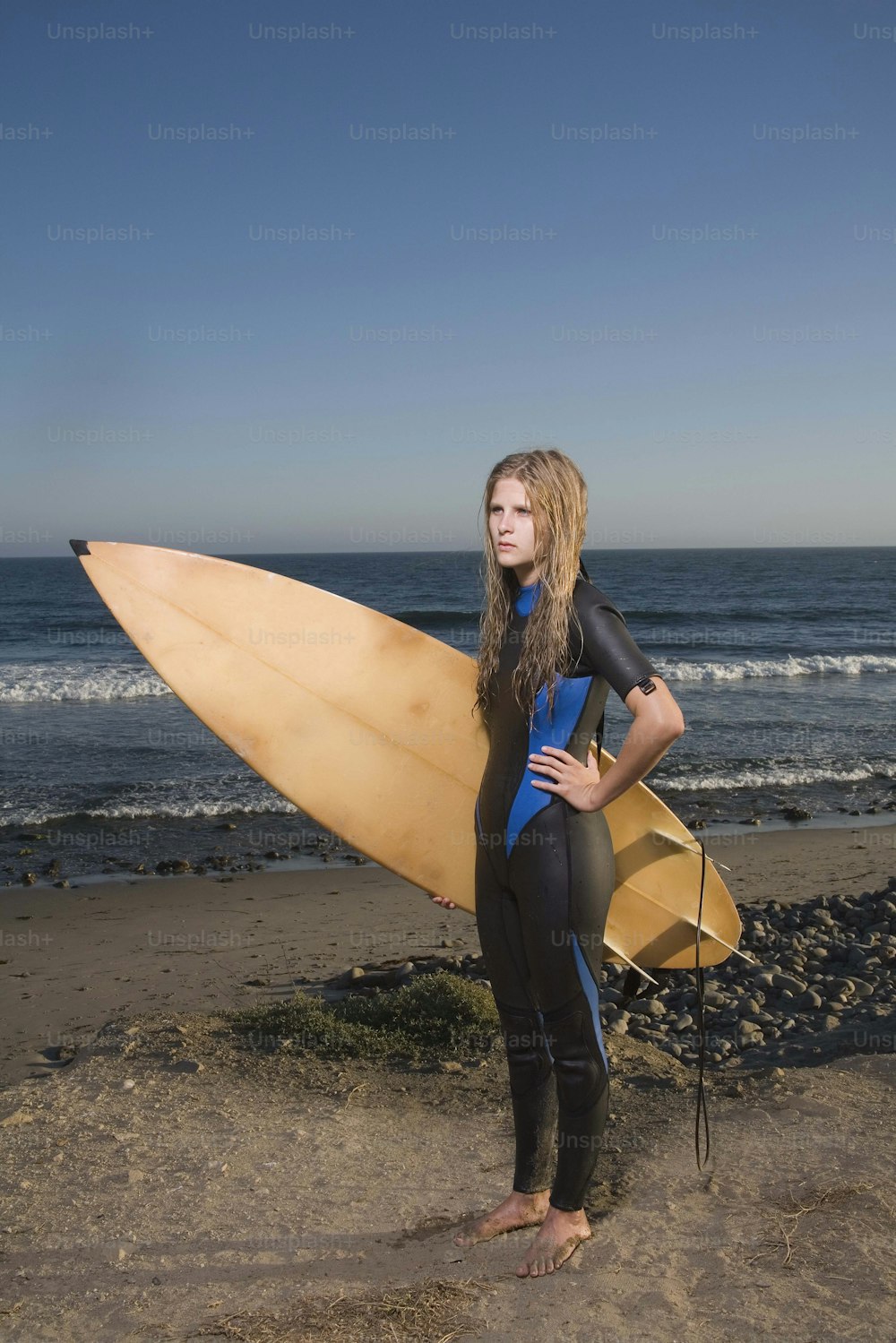 uma mulher em pé em uma praia segurando uma prancha de surf