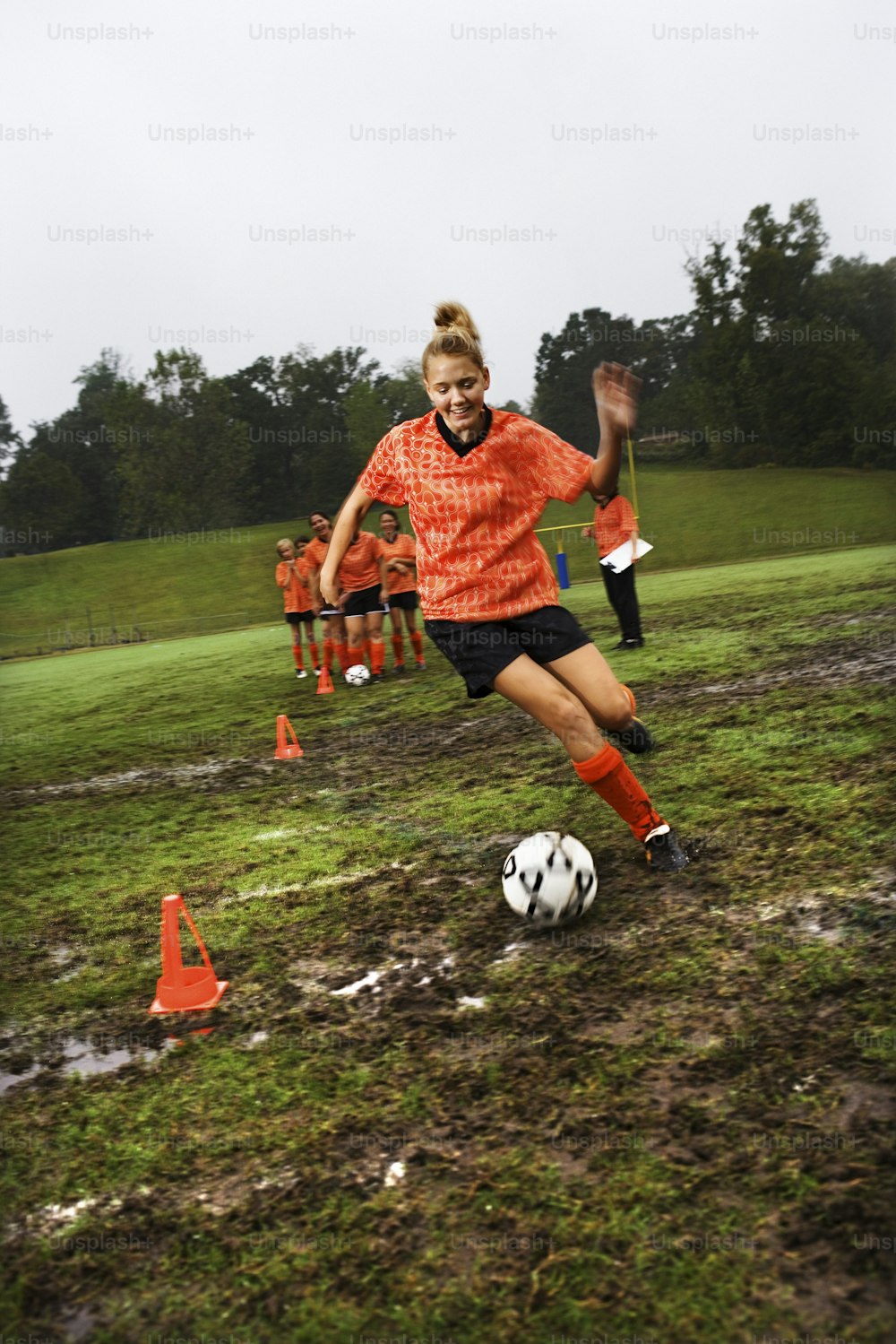 a girl in an orange shirt is kicking a soccer ball