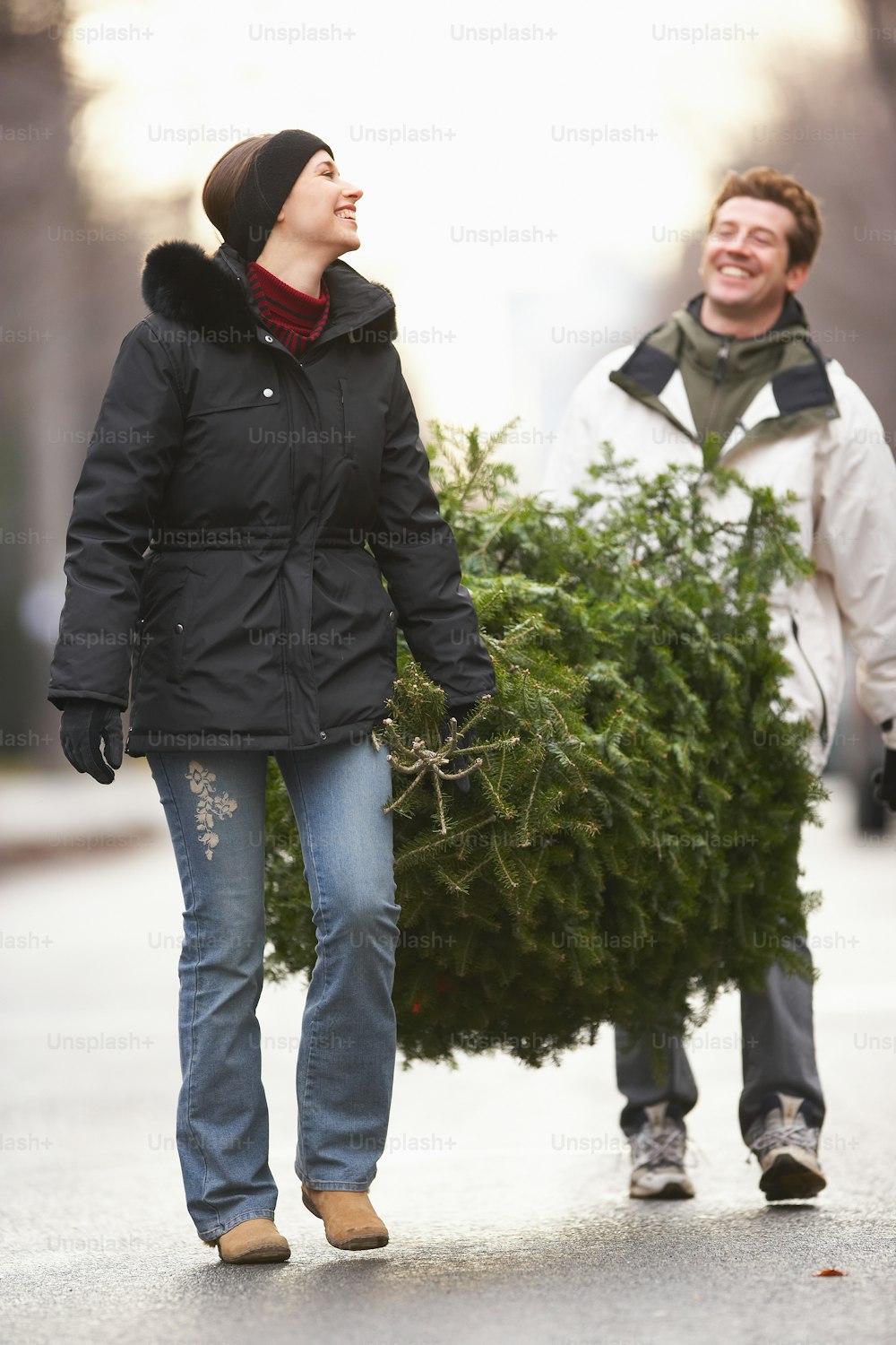 a man and woman walking down a street carrying a christmas tree