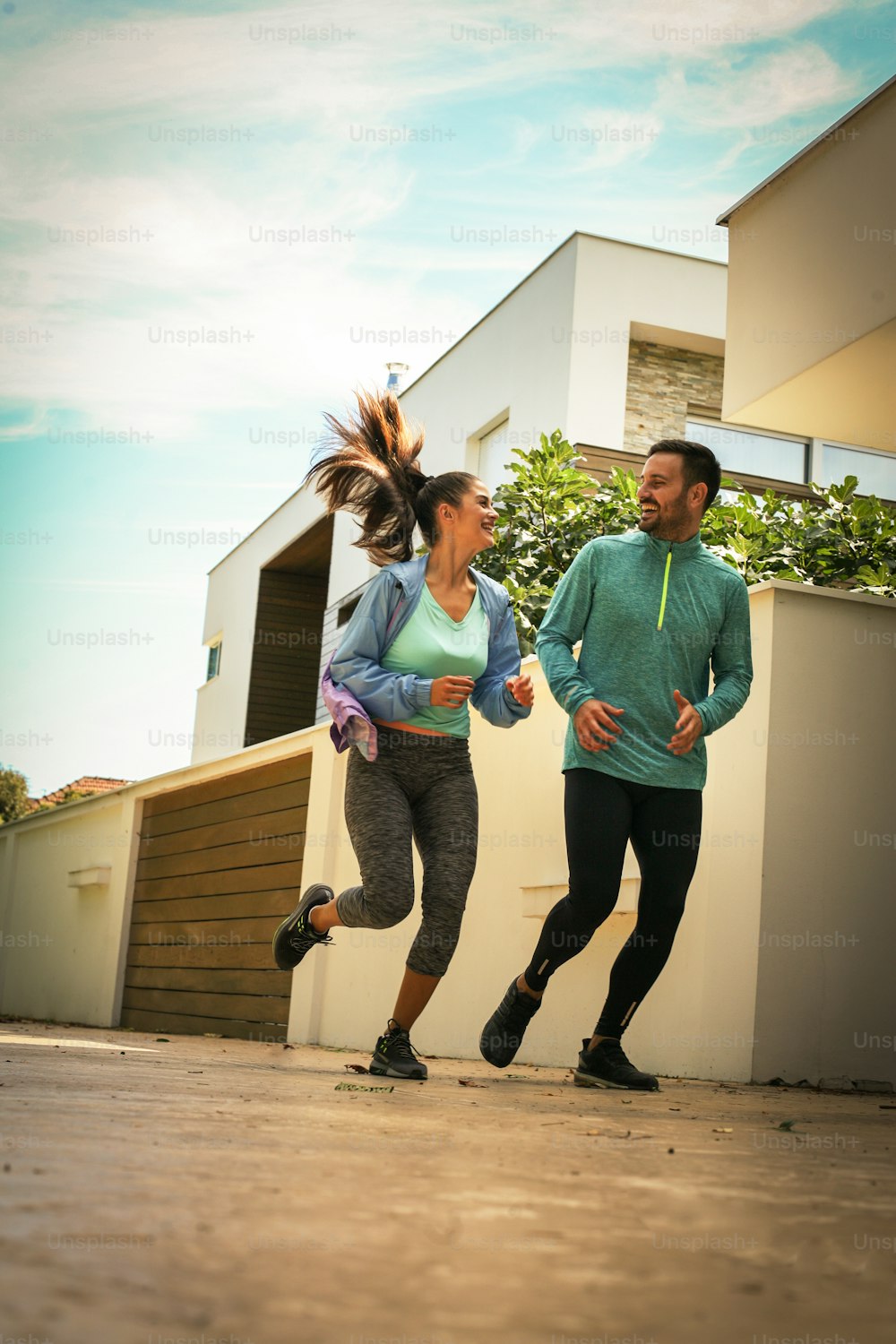 Young couple running together on sidewalk. Young people exercising.
