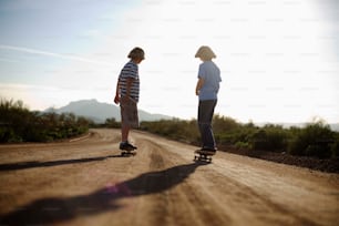 a couple of people riding skateboards down a dirt road