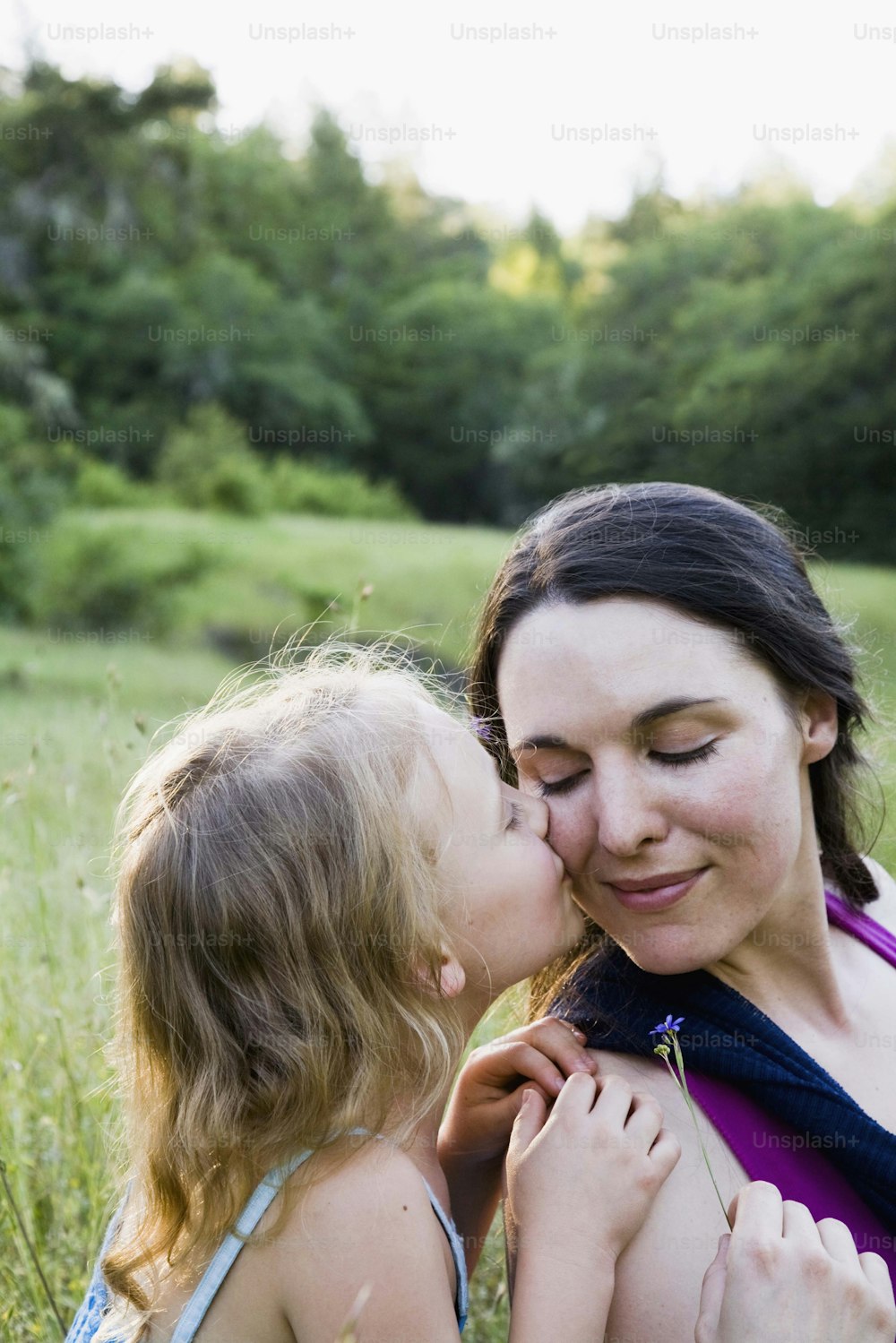 a woman kissing a little girl in a field