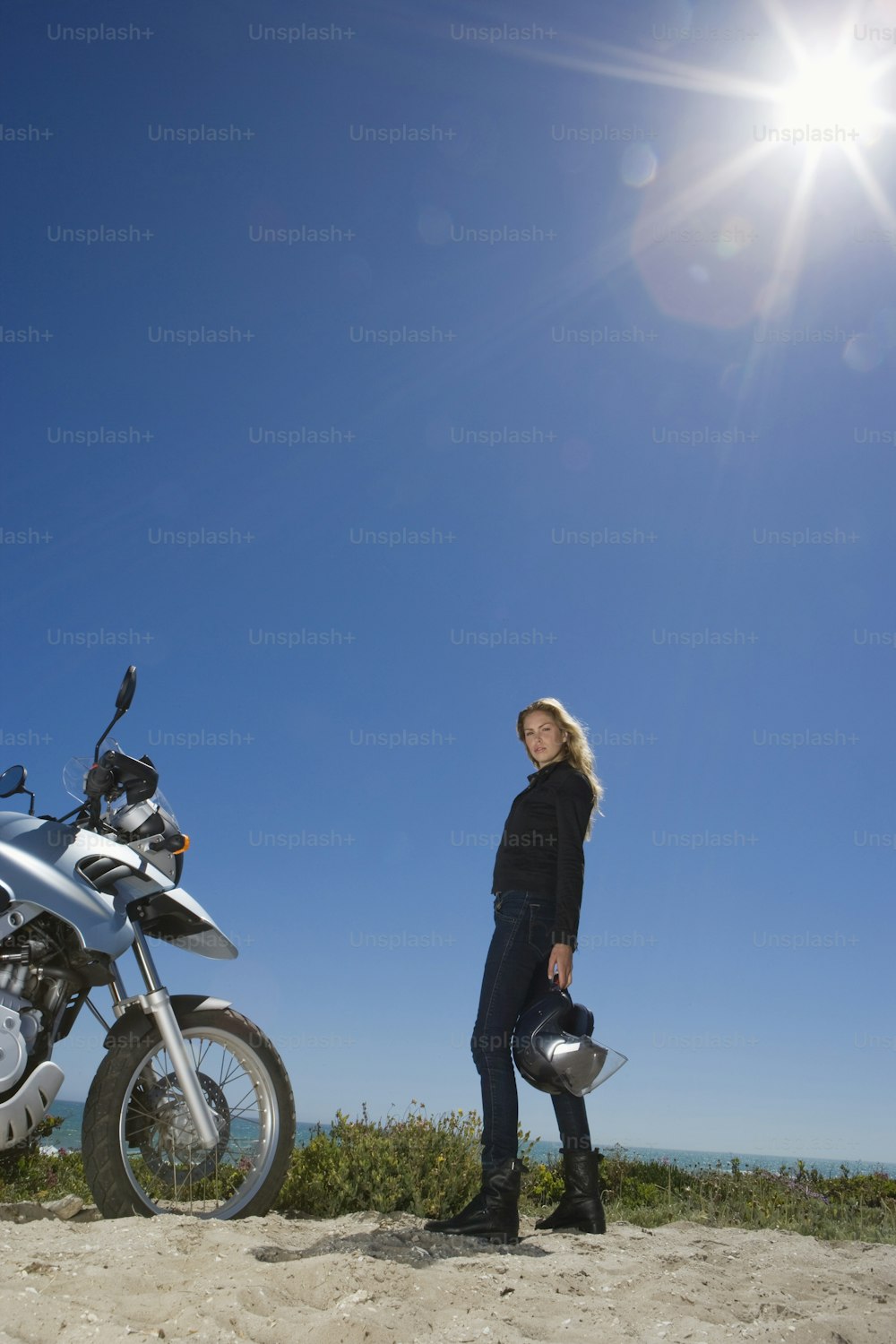 Una mujer parada junto a una motocicleta en una playa