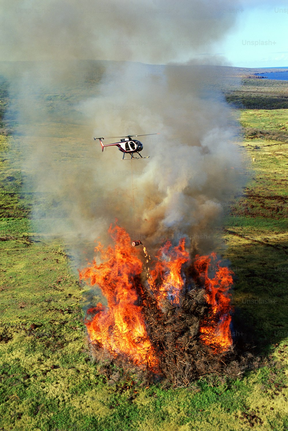 野原の大火の上を飛ぶヘリコプター