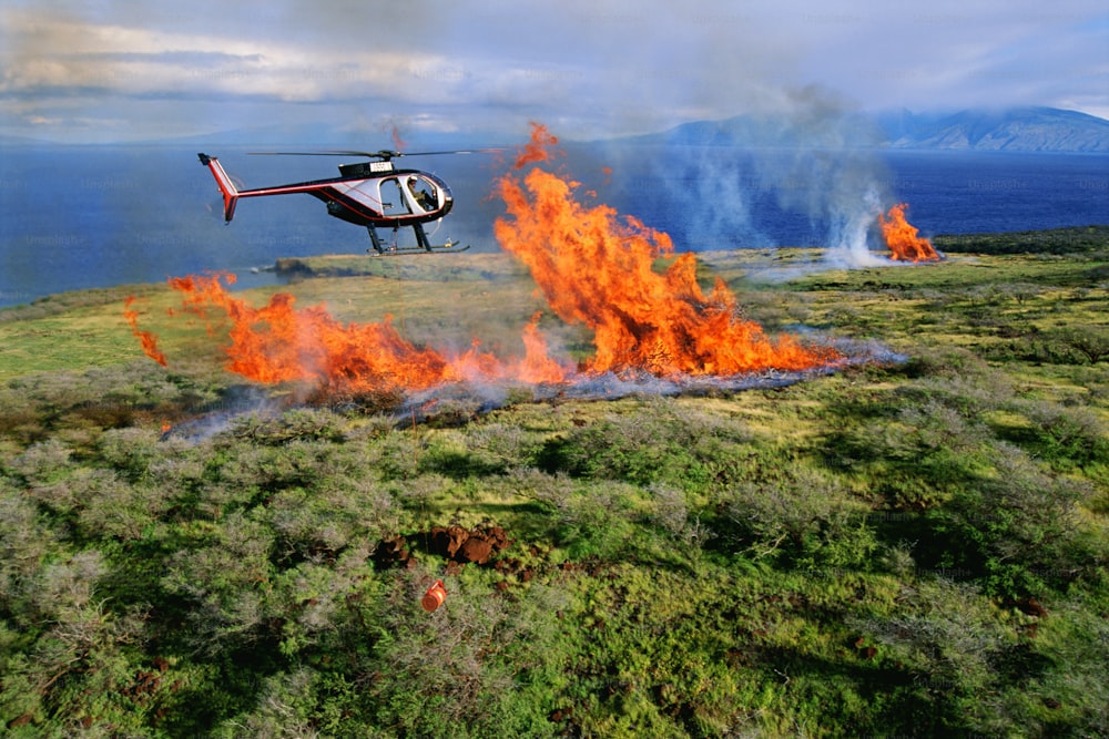 a helicopter flying over a field on fire
