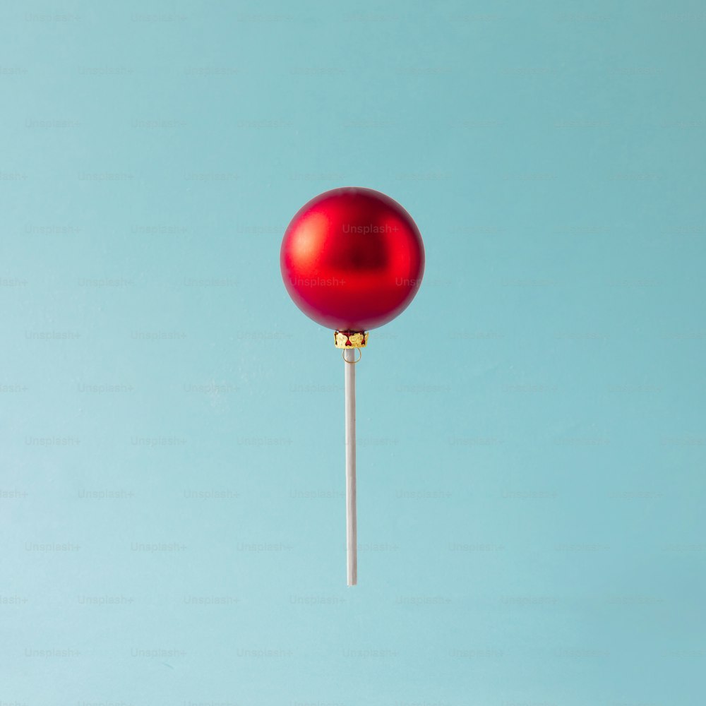 Piruleta hecha de bola navideña roja sobre fondo azul. Concepto de dulces navideños.