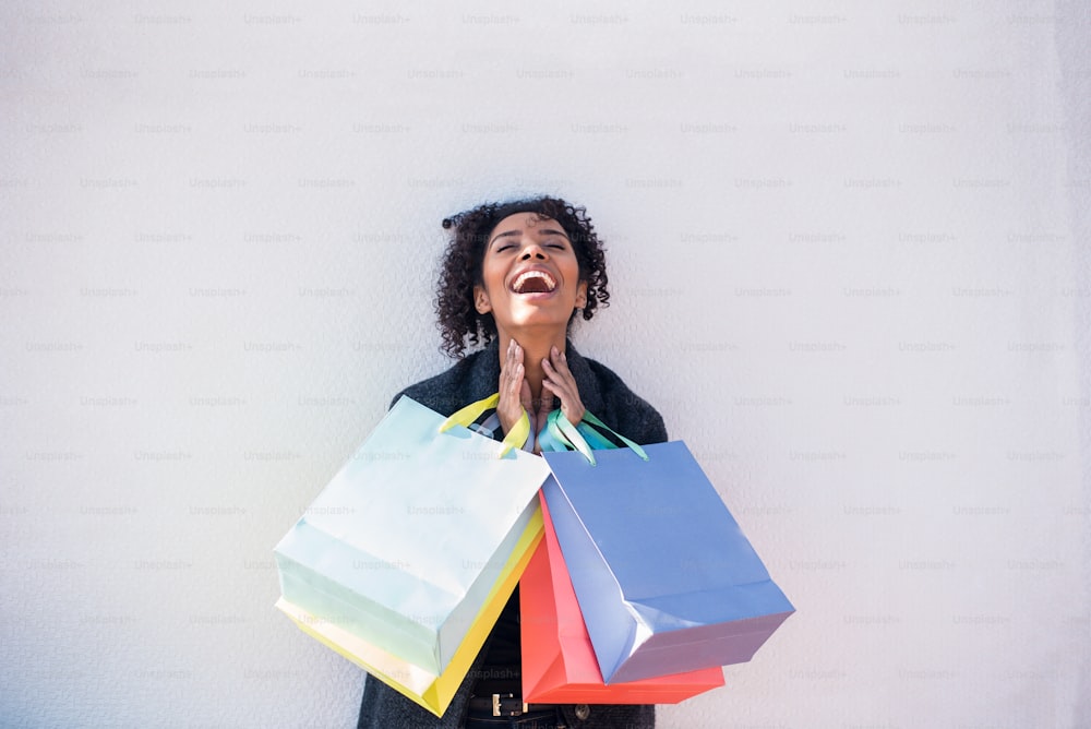 Happy young black woman with shopping bags against a white wall