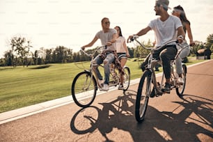 Gruppo di giovani felici in abbigliamento casual sorridenti mentre pedalano insieme all'aperto