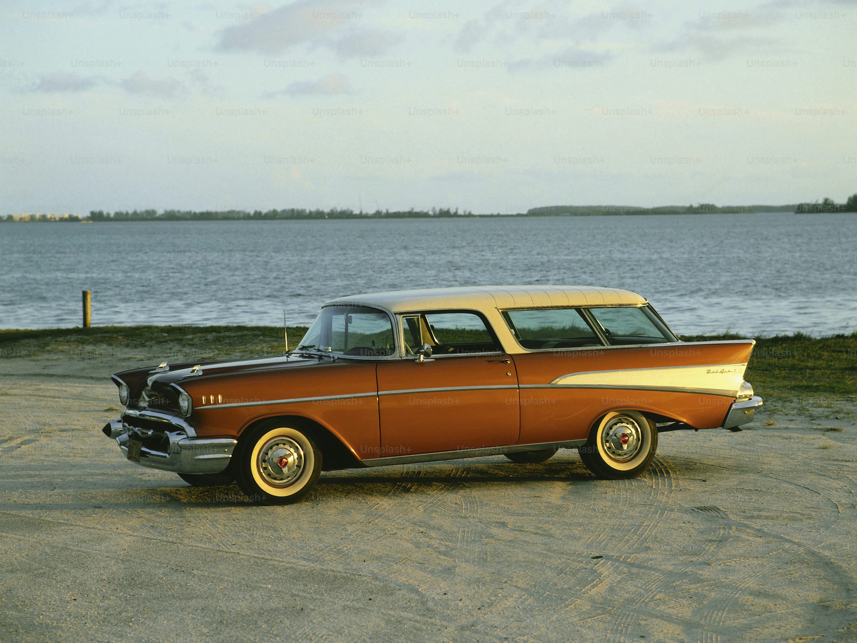 an orange and white car parked in front of a body of water