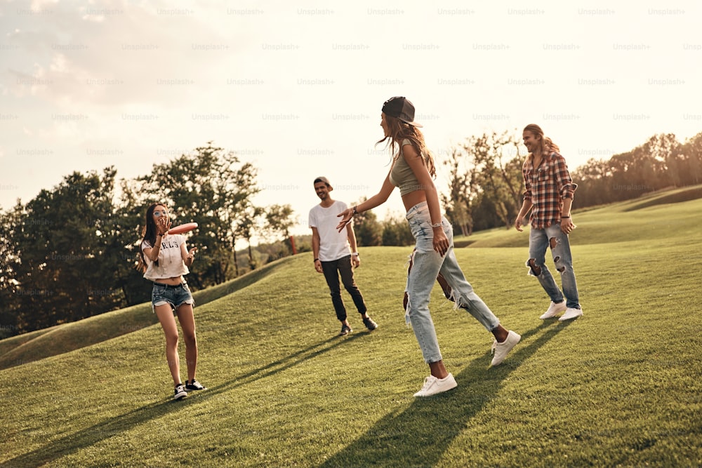 Longitud completa de jóvenes sonrientes en ropa casual jugando al frisbee mientras pasan tiempo despreocupado al aire libre