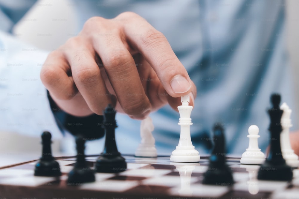 체스 게임 플레이어는 흰색 폰을 한 걸음 앞으로 움직입니다. 파란색 배경에 보드에 체스 조각. 체스맨은 체스를 두며 첫 번째 동작을 폰으로 만들고 손을 보여줍니다.