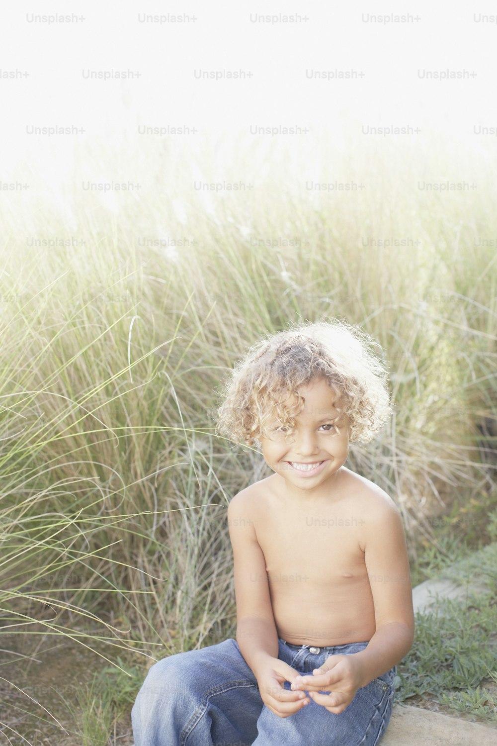 a young boy sitting on a rock in front of tall grass