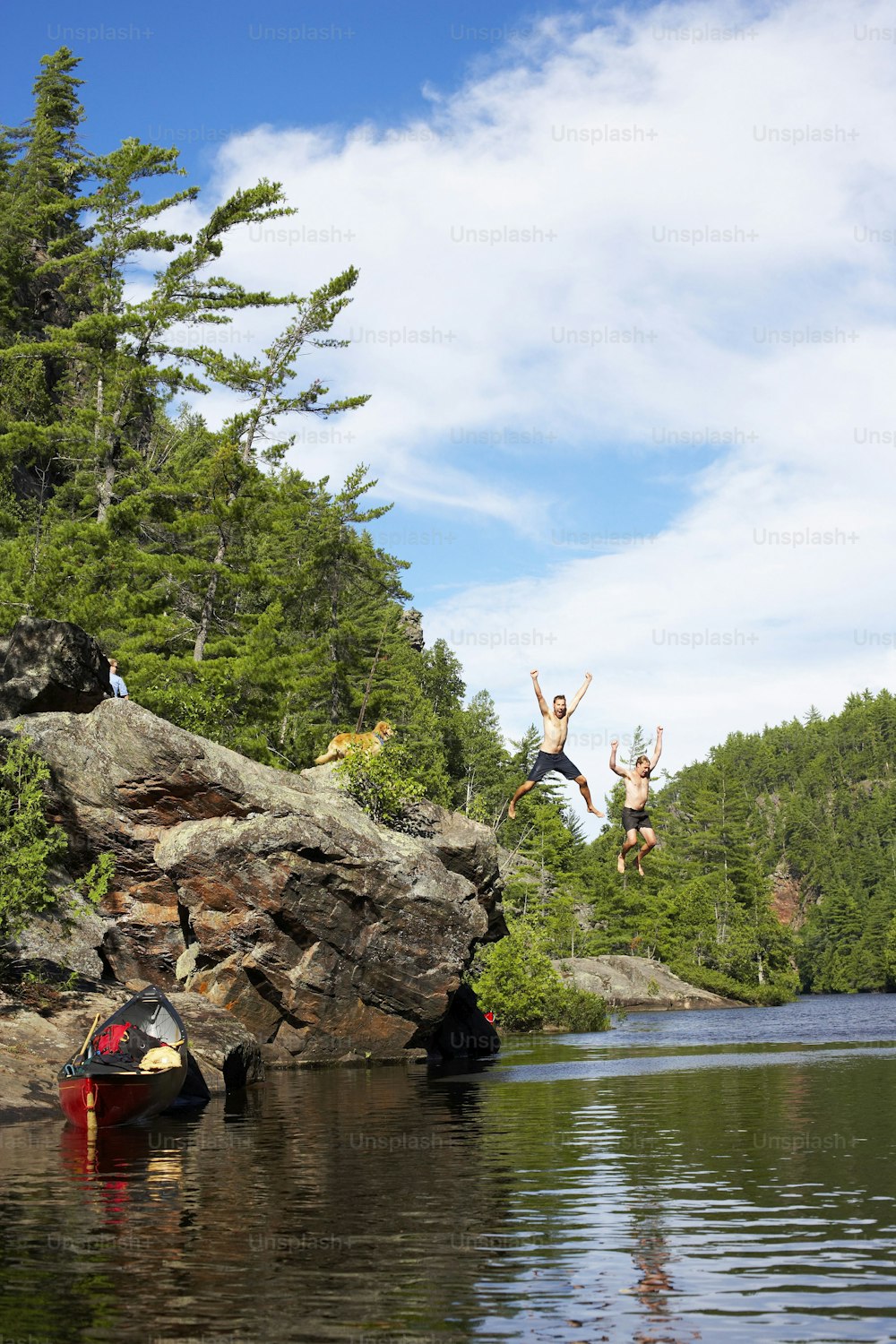 duas pessoas pulando de pedras em um lago