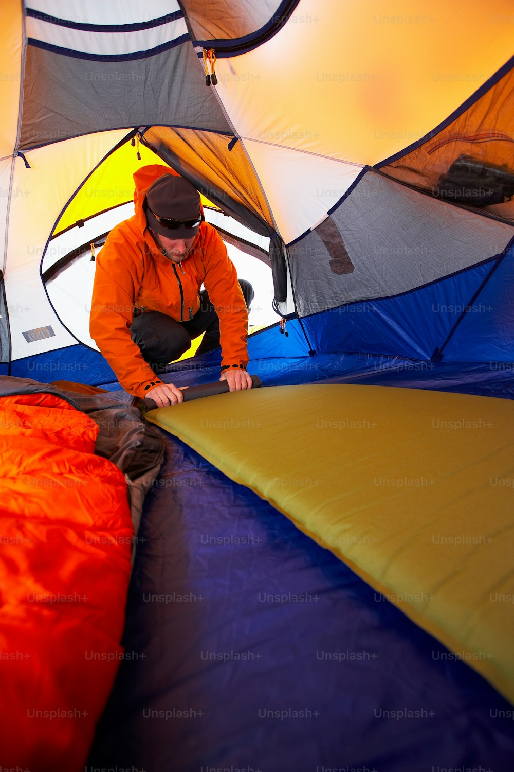Un uomo in giacca arancione che monta una tenda blu e gialla