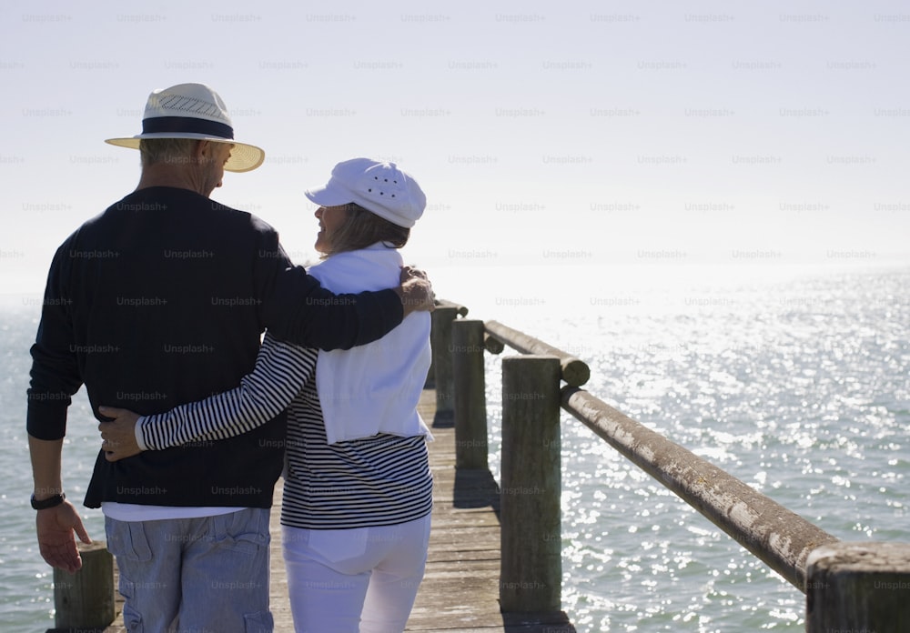 a man and a woman standing on a pier next to the ocean