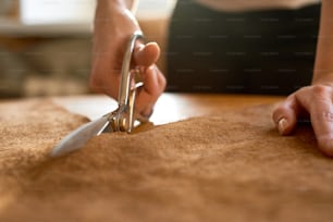 Artigiano femminile che taglia la pelle marrone con le forbici da vicino