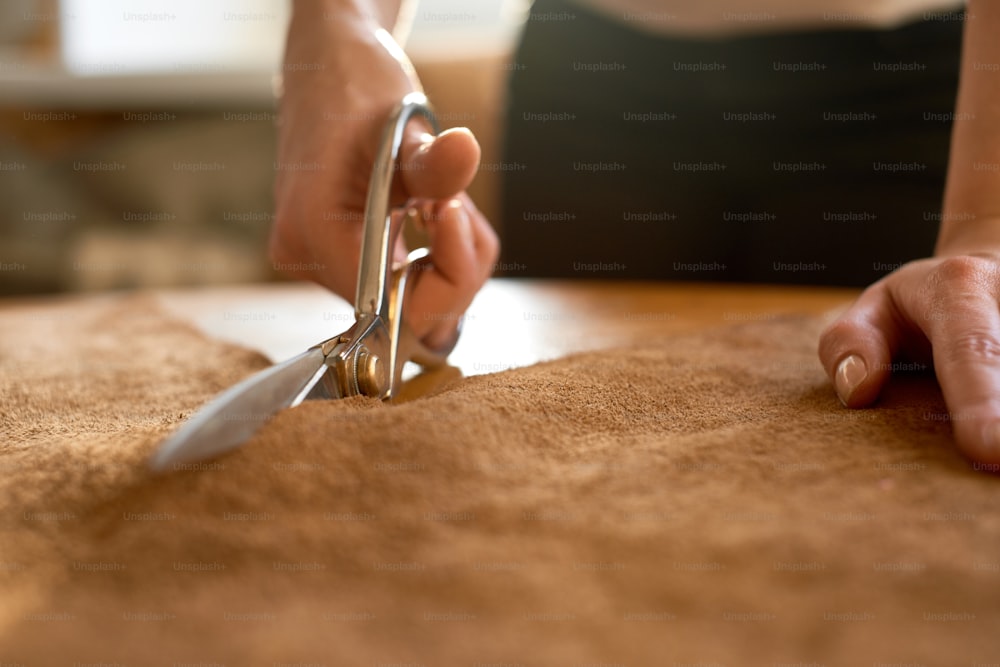 ハサミで茶色の革を切る女性職人の接写