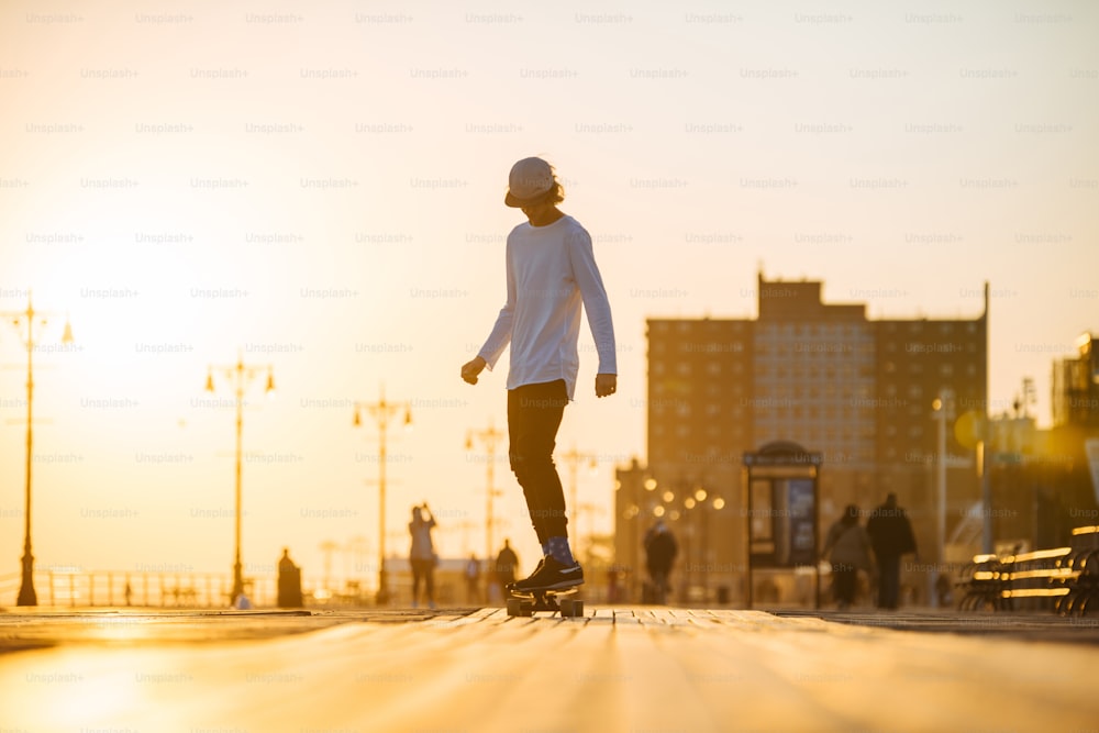 Junger Skaterboy fährt Longboard auf der Promenade, Silhouette bei Sonnenuntergang
