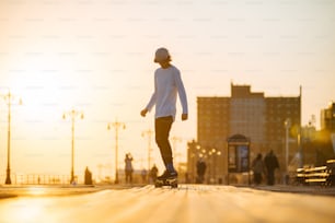 Jeune skaterboy équitation longboard sur la promenade, silhouette sur le coucher du soleil