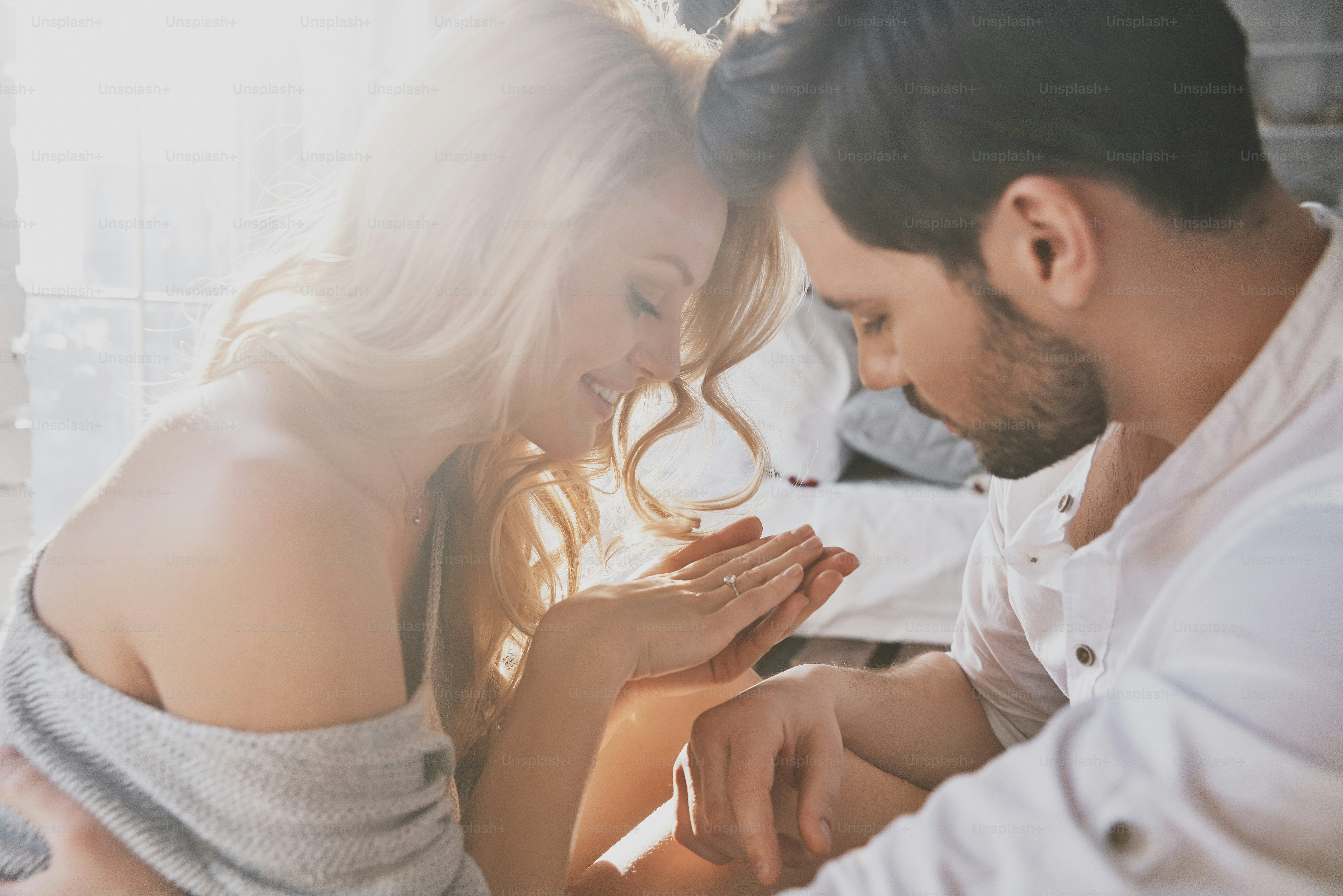 Beautiful young woman looking at her engagement ring and smiling while sitting in the bedroom with her boyfriend