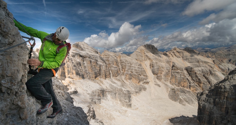 イタリアのドロミテの南チロルの素晴らしい景色を望む急で露出したフェラータ通りの男性登山者