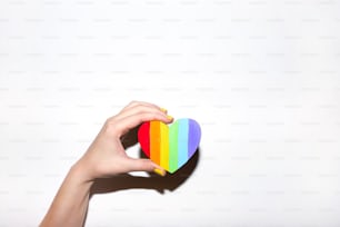 Cuore a forma di cuore di simbolo dell'orgoglio gay arcobaleno nelle mani su bianco