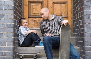 a man sitting next to a boy holding a skateboard