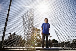 a young man holding a skateboard next to a fence