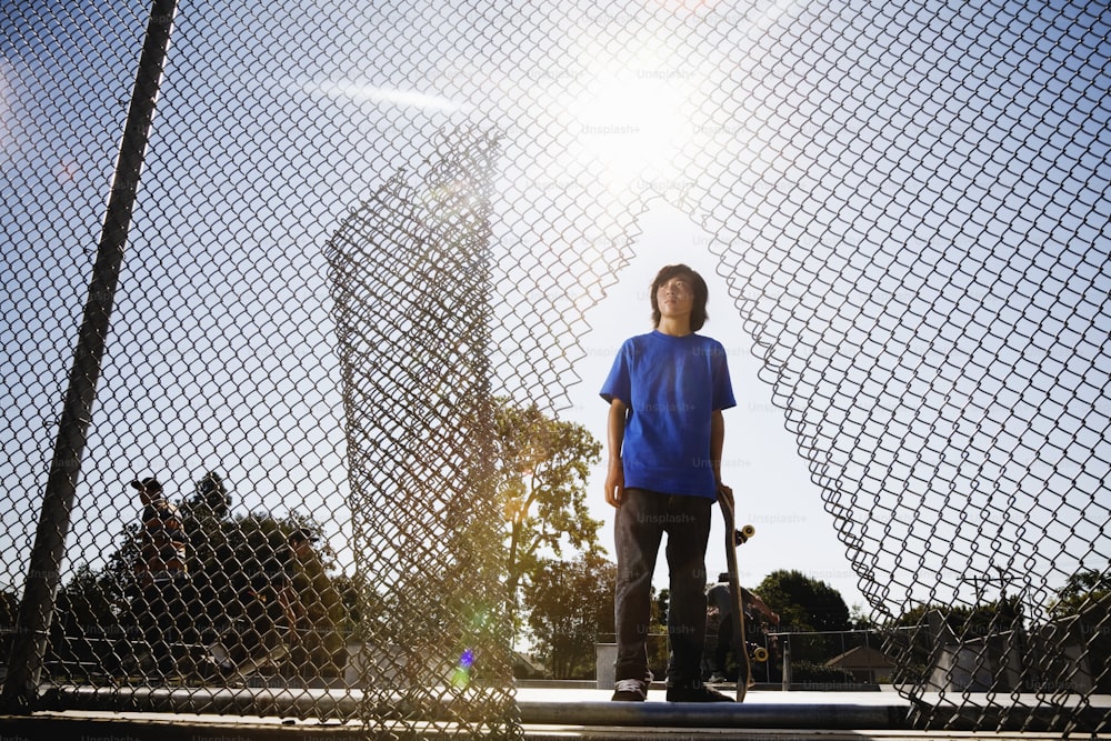 a young man holding a skateboard next to a fence
