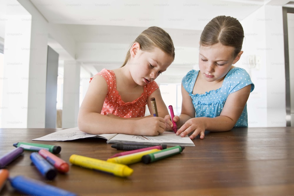two young girls sitting at a table with crayons